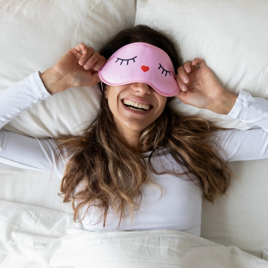 Happy millennial woman lying in bed with sleeping mask | Bow Family Furniture & Flooring